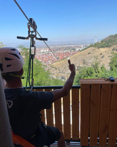 A rider clipped to the cable gives a thumbs-up, the city ahead